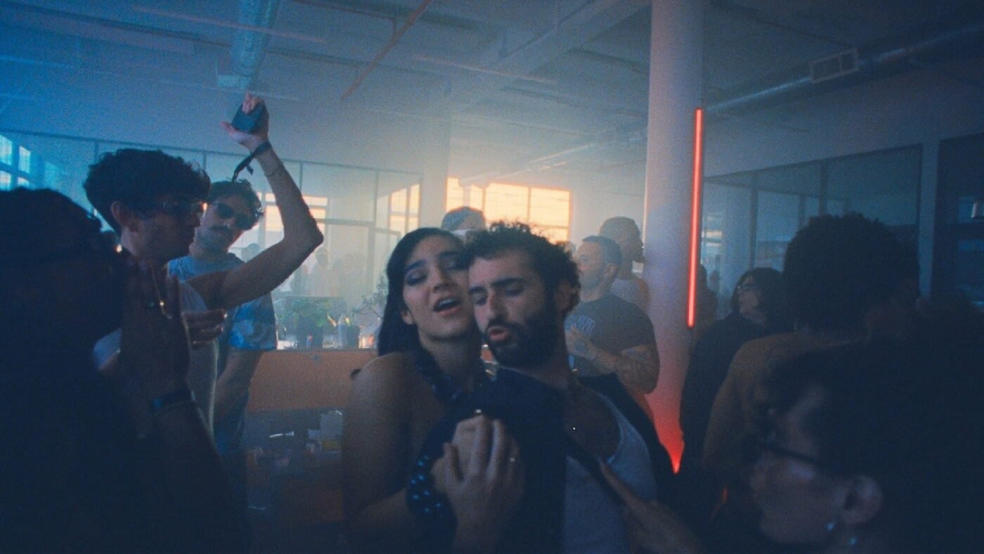 Una fiesta nocturna en un loft con humo y luz azul, con dos personas bailando abrazadas en primer plano