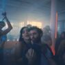 Una fiesta nocturna en un loft con humo y luz azul, con dos personas bailando abrazadas en primer plano