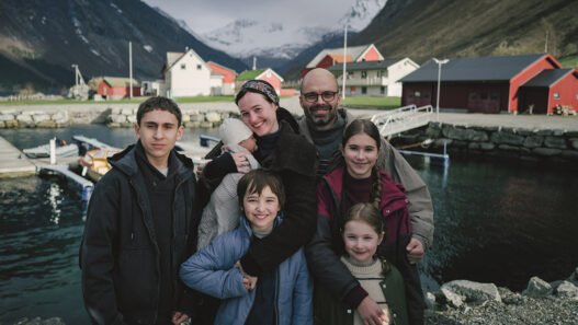 Una familia con cinco hijos posa sonriendo frente a un fiordo noruego en Fjord