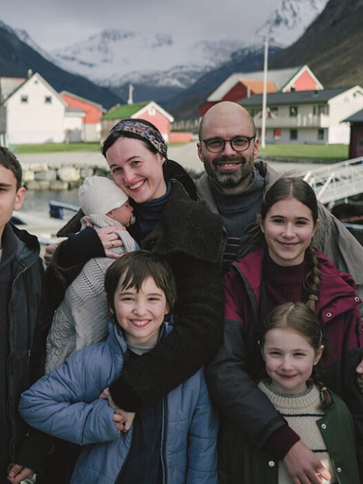 Una familia con cinco hijos posa sonriendo frente a un fiordo noruego en Fjord