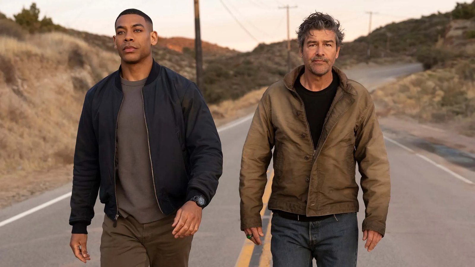 Kyle Chandler y Aaron Pierre caminando por una carretera en Lanterns