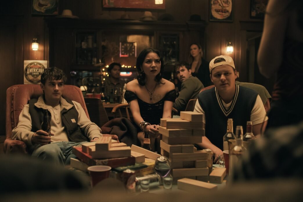 Personajes de Obsession sentados alrededor de una mesa con una torre de bloques de madera