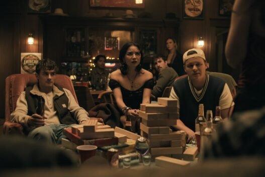 Personajes de Obsession sentados alrededor de una mesa con una torre de bloques de madera