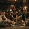 Personajes de Obsession sentados alrededor de una mesa con una torre de bloques de madera