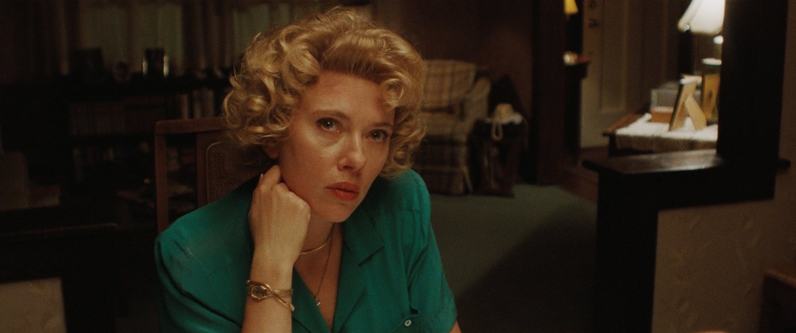 Scarlett Johansson como Hester, con peinado rizado y blusa verde, sentada en la sala de su casa