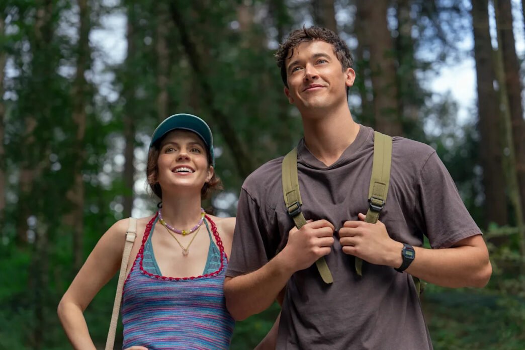 Emily Bader y Tom Blyth caminando por un bosque con mochilas en People We Meet on Vacation