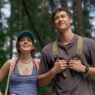 Emily Bader y Tom Blyth caminando por un bosque con mochilas en People We Meet on Vacation