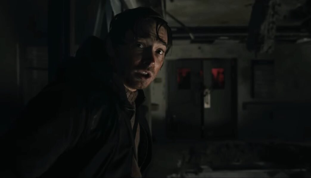 Austin Abrams en la penumbra de un pasillo en Resident Evil