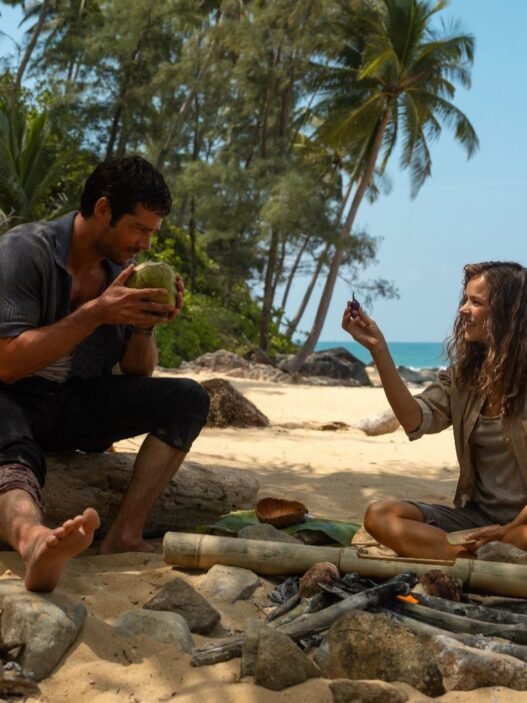 Dylan O'Brien y Rachel McAdams sentados en una playa en Send Help