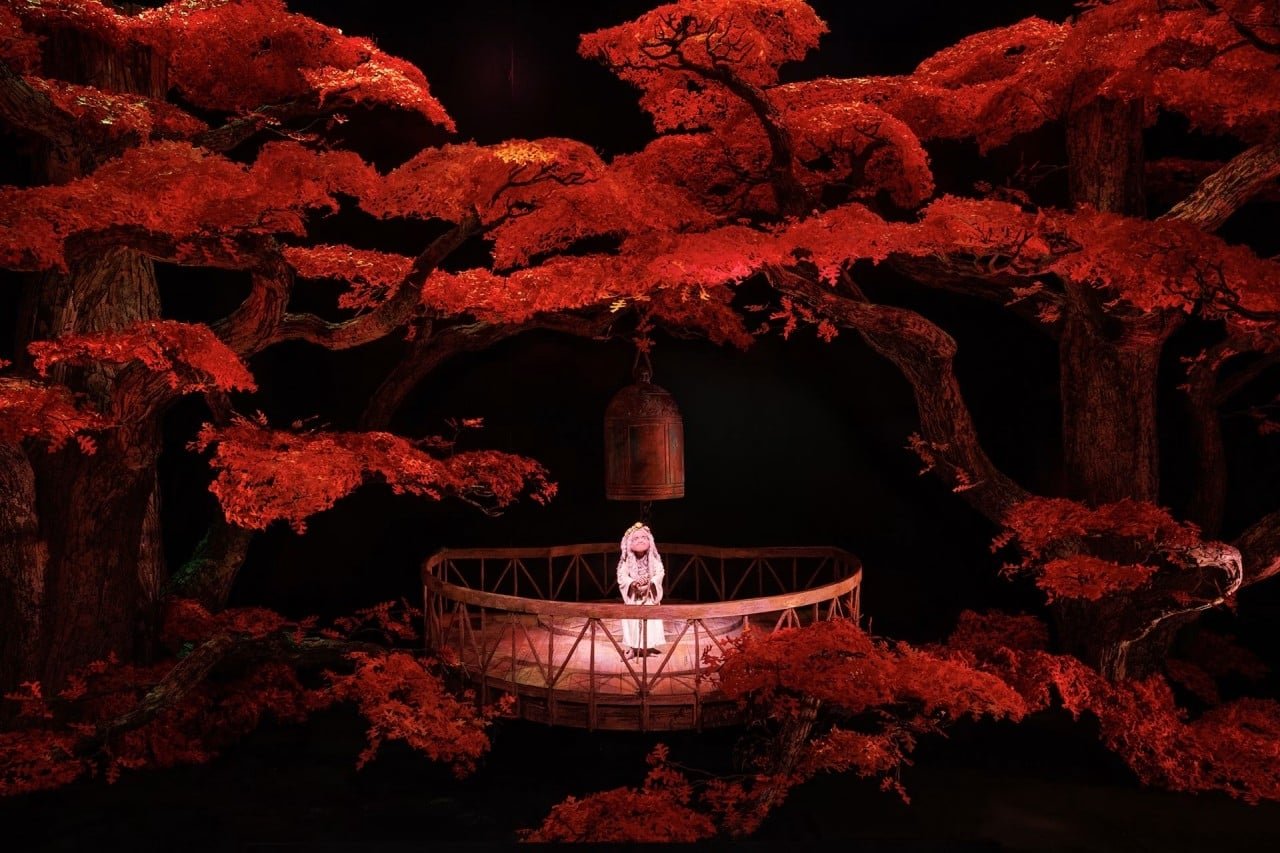 Miniatura iluminada de un bosque de árboles rojos con una campana colgada y una figura pequeña en un balcón